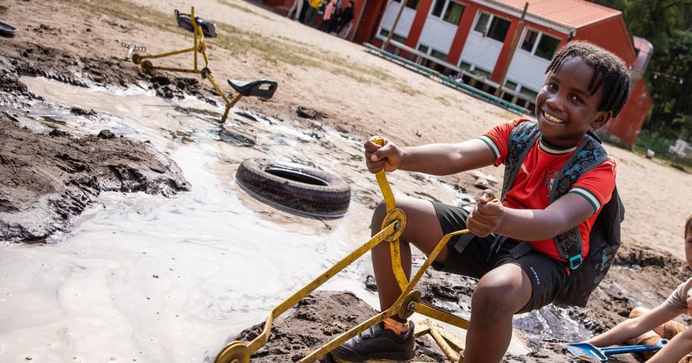 kind speelt met kraan in zandbak en heeft rugzak aan