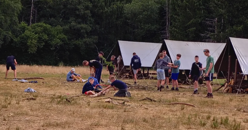 Foto van een tenten op een veld en spelende kinderen die met de jeugdvereniging op kamp zijn