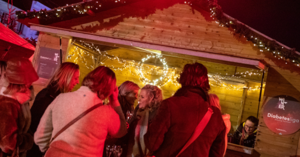 Mensen drinken iets bij een standje op de kerstmarkt